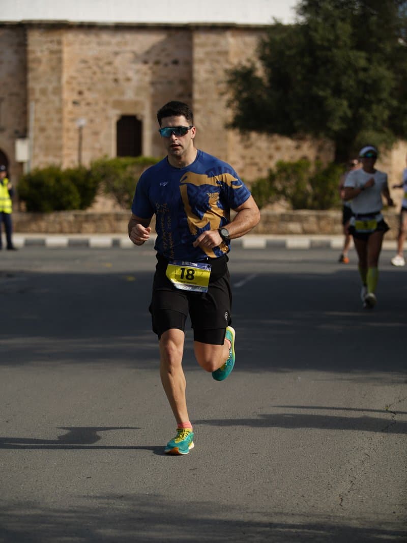 Coach Stefan racing on the road in Cyprus, passing a stone building