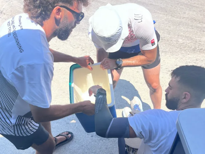 Crew taping the athlete's lower leg beside the van in midday heat