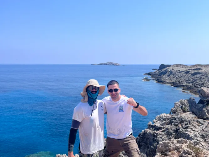 The athlete and a crew member on rock above blue sea, an islet offshore