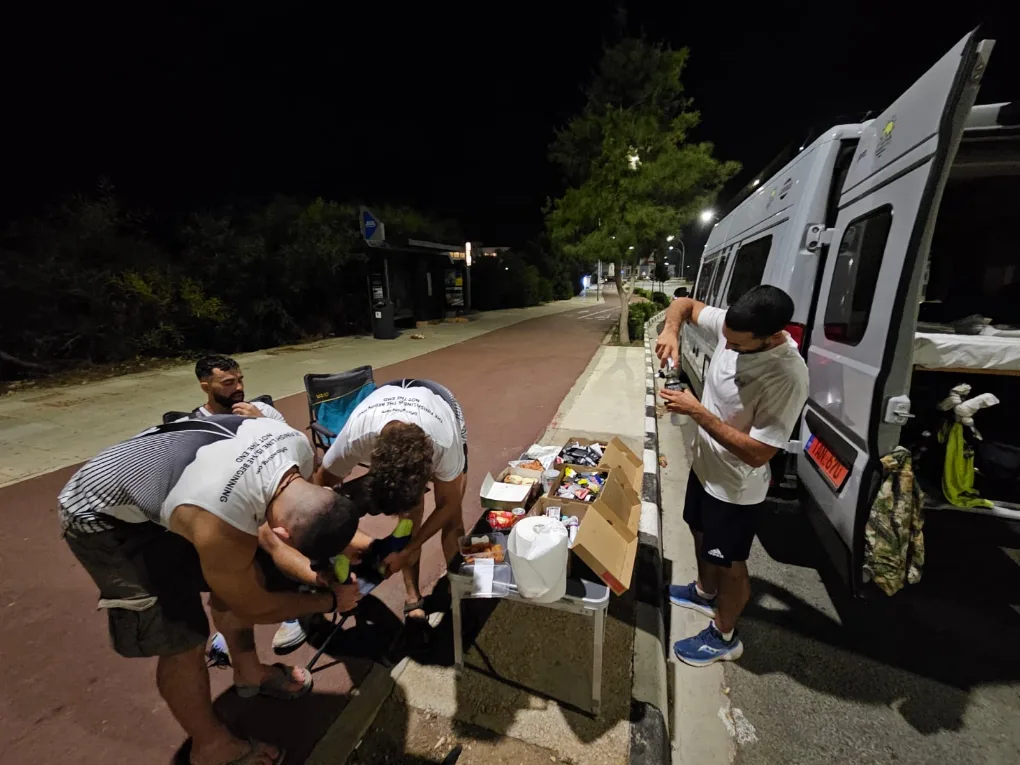 A night stop on a coastal road, the van open with supplies laid out on a table beside it