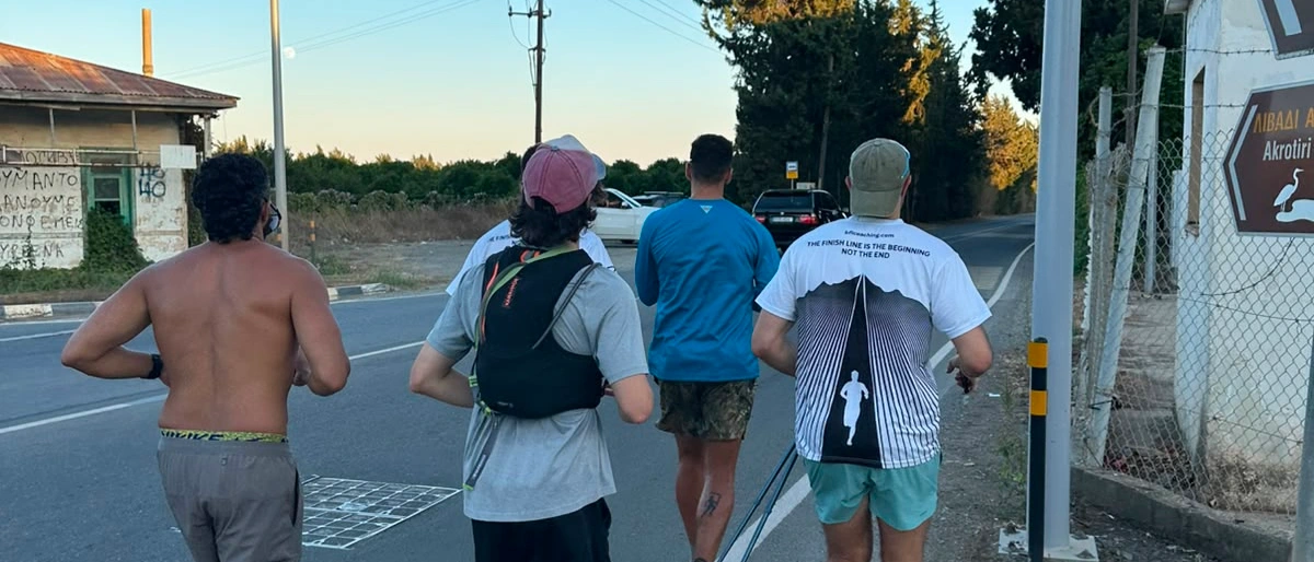 Four runners seen from behind on a road at first light, one carrying a pack
